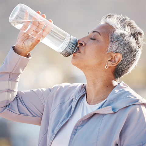 Woman with short hair in a light jacket drinks water outdoors