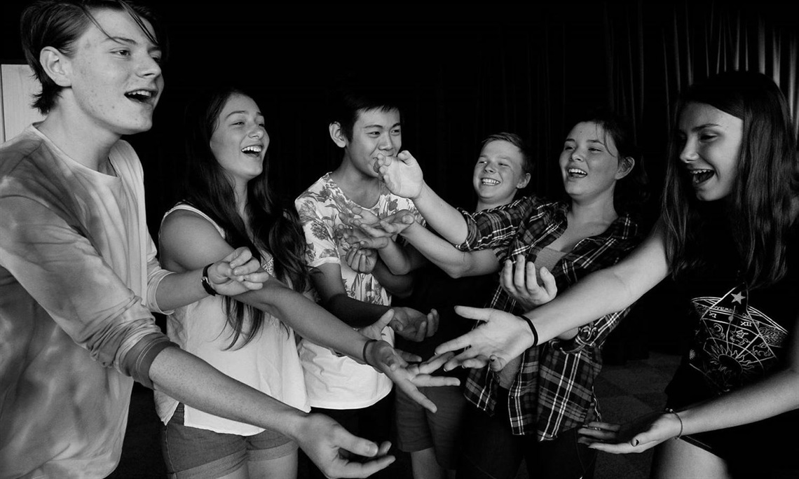 Black and white image of six teenagers laughing and extending their hands towards each other in a playful and joyful manner, conveying friendship.
