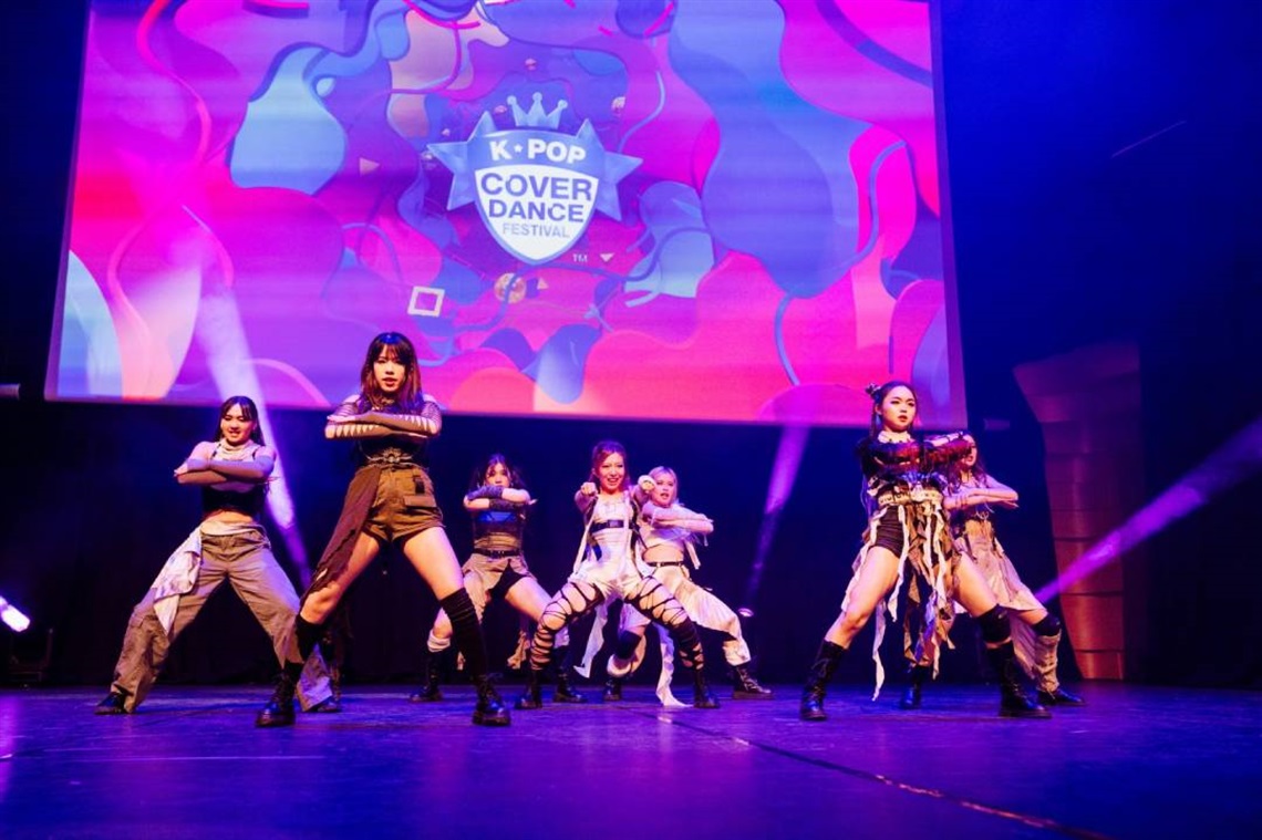A group of dancers perform energetically on stage at a K-Pop Cover Dance Festival.
