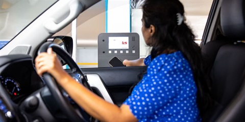 A woman sits in a parked car at a ticketing machine, paying a parking ticket.
