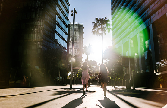 image of two girls running away from the camera towards the sun, between high rise buildings