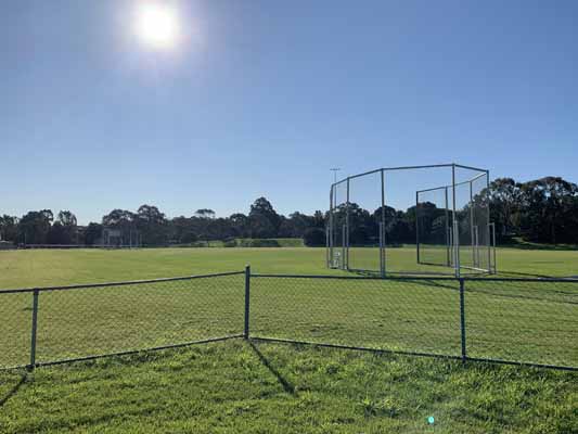 Image of Barton Park and the shot put throwing cage which is one of the park's many features. Perfect sunny day with blue sky and lush green grass. 