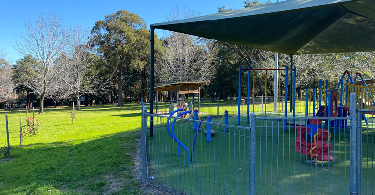 Playground on right with sensory equipment with shade cloth, grass on left