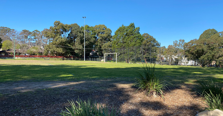 Sports field with soccer goal, high fence and amenities building in background