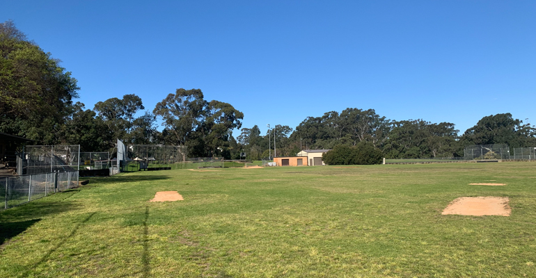 Sports field with sand patches with fencing and amenities building in far background