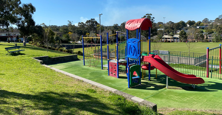 Play space with slide and climbing equipment on hill, fencing and sports field to the back