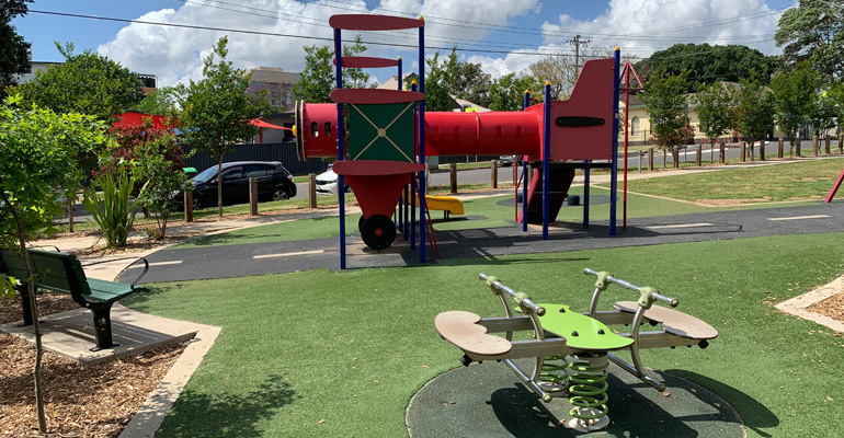 Play equipment in shape of airplane, rocker in front and park bench on left