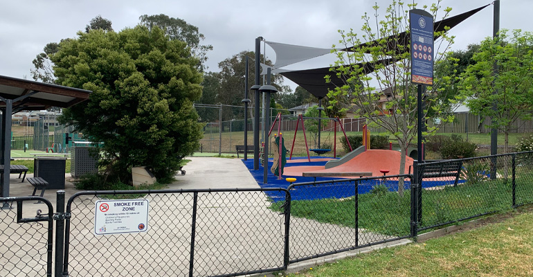 Metal fence with picnic area, courts in background, play ground with hill slides and giant swing 