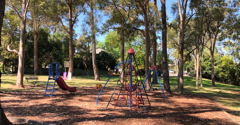 Playground with slide, climbing nets and swings surrounded by trees