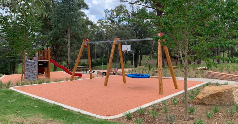 Swings, slide with rock climbing wall, picnic table and benches and basketball court in background