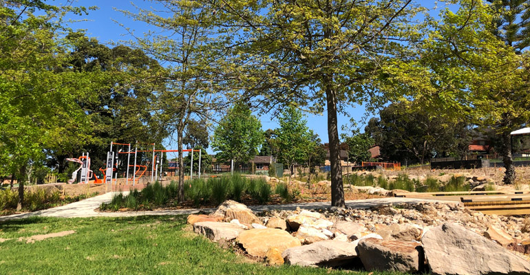 Park with sandstone rocks, grass, trees and play equipment in background