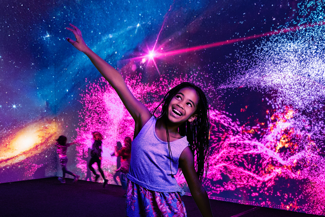 Girl with hand in the air smiling in front of galaxy backdrop