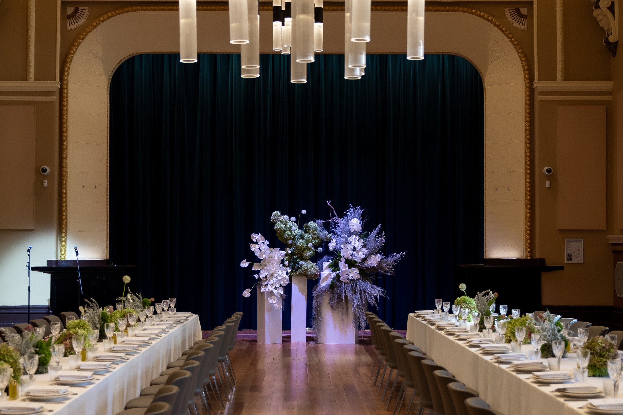 Long tables with dining set up, large floral arrangement at the front of the hall