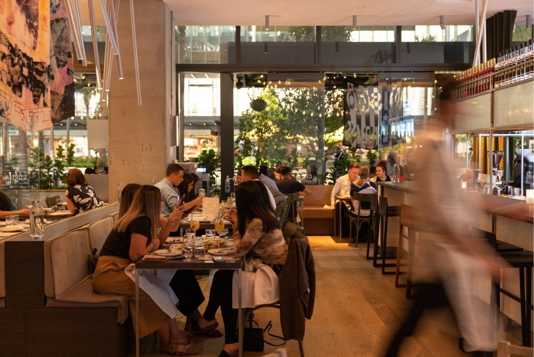 Image of a bustling restaurant full of people and a waiter swiftly walking by