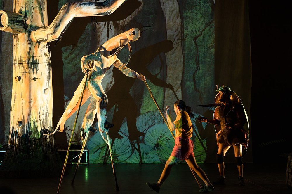 Person on stilts with the girl and beetle on stage