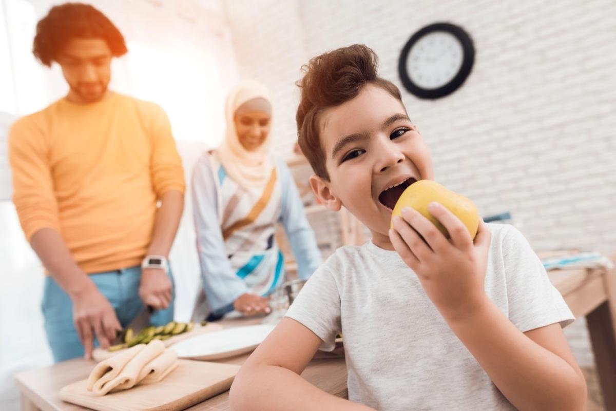 Child eating apple in kitchen with parents
