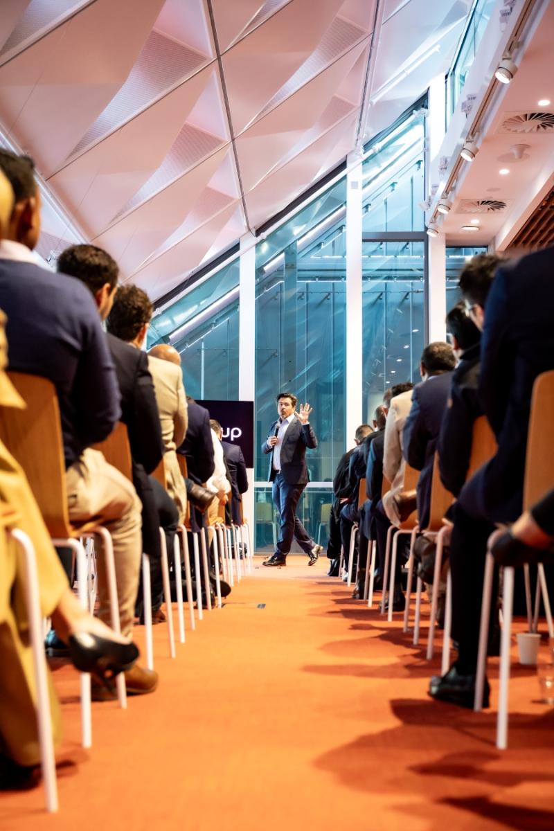 People sitting with their backs to the camera looking at man with hand up holding microphone
