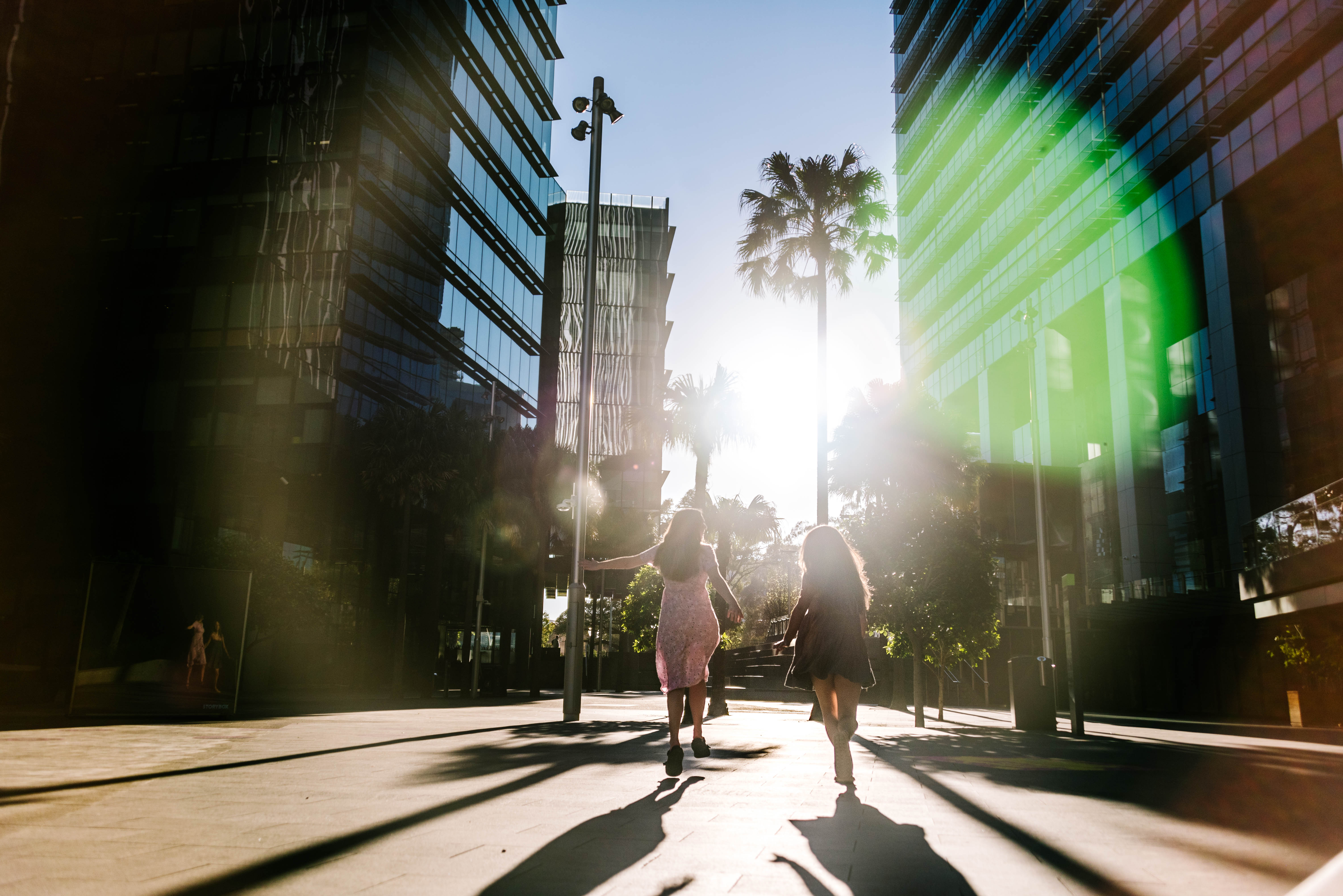 image of two girls running away from the camera towards the sun, between high rise buildings