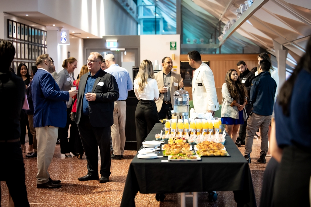 People standing in atrium with tables with black table cloths and food and drink