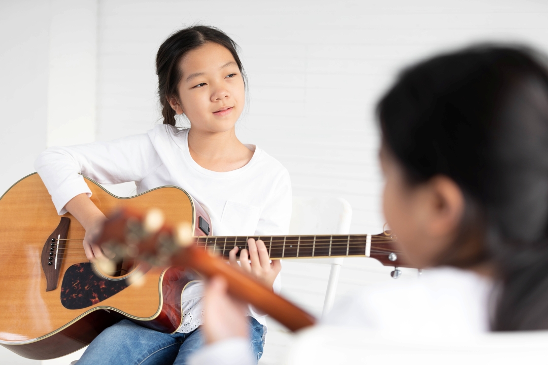 Little girl in white long sleeve tshirt holding acoustic guitar