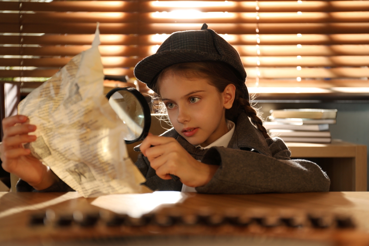 Girl in detective hat holding map and magnifying glass