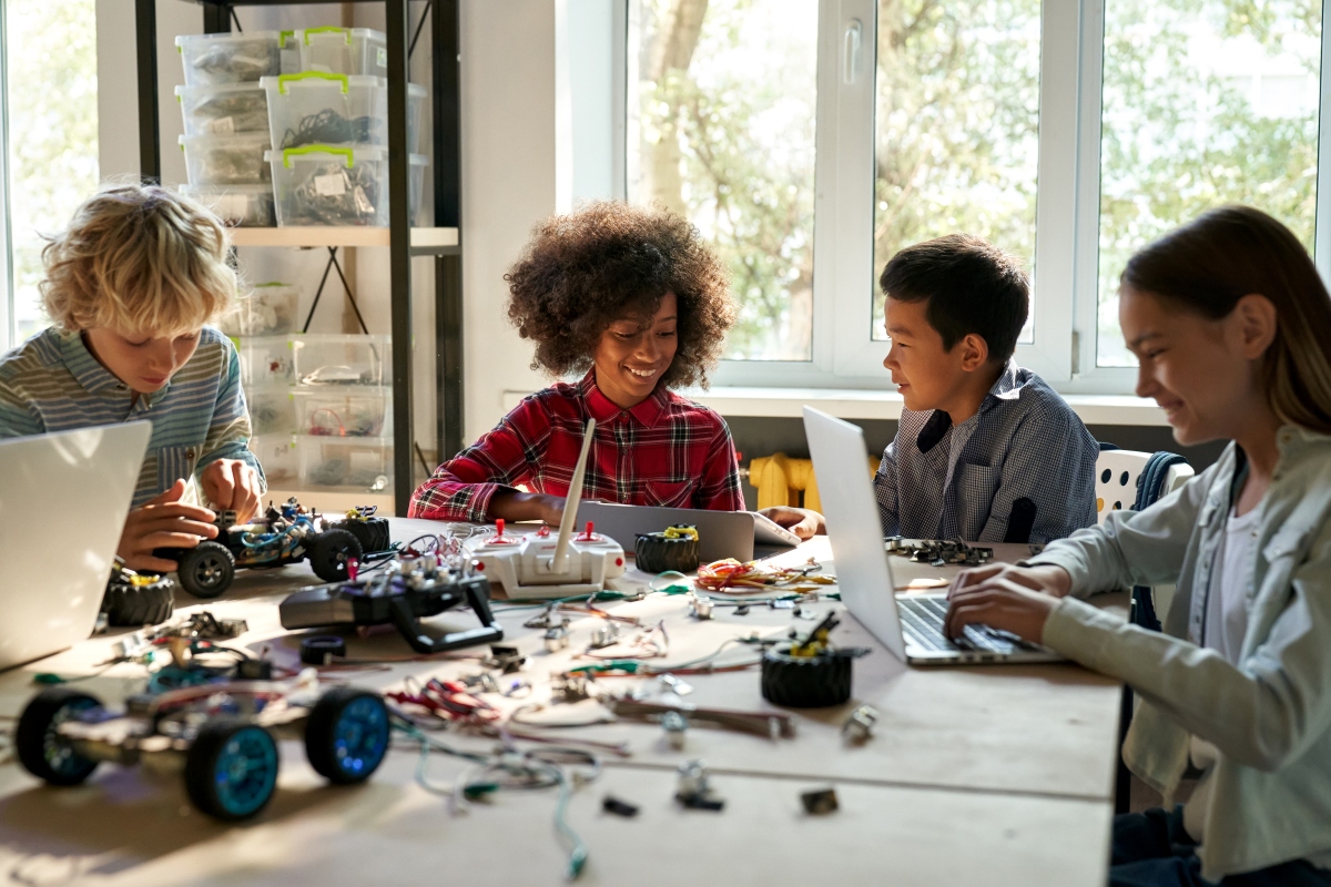 4 children sitting at desk with computers and electronic parts