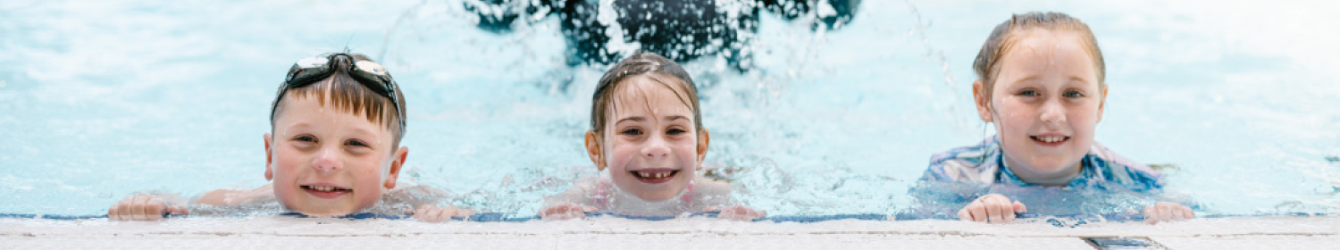 three young swimmers in pool smiling to camera