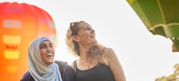 Two Woman in park with hot air balloons in back ground