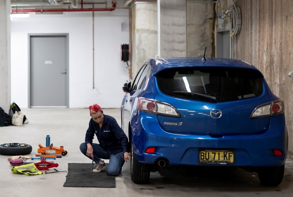 Woman crouching beside a blue mazda